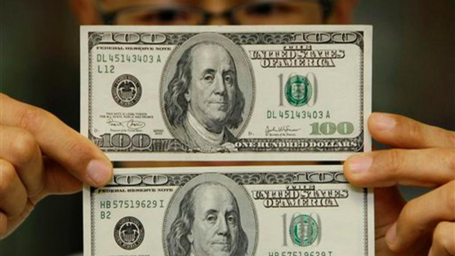 Seorang pakar membandingkan uang dolar asli (bawah) dengan yang palsu (atas)