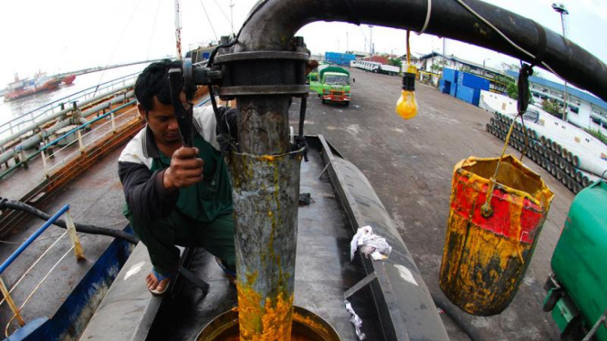 Pekerja sedang memasukkan minyak sawit (CPO) ke kapal tongkang.