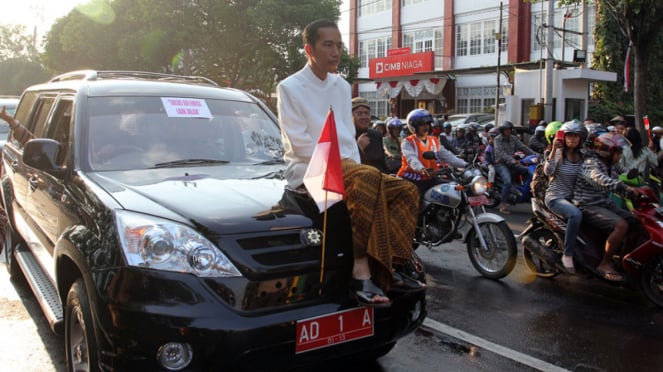 Joko Widodo duduk di atas kap mesin mobil Esemka yang telah dinyatakan lolos uji emisi. Saat itu Jokowi masih menjabat Wali Kota Solo.