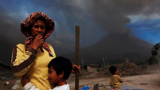 Seorang ibu dan anaknya dengan latar belakang letusan Gunung Sinabung
