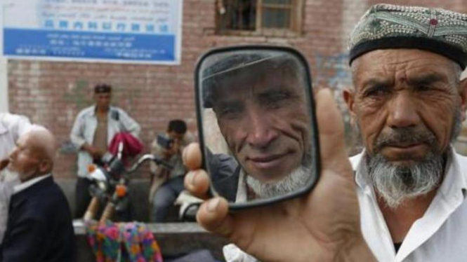 Seorang pria di Urumqi, Xinjiang, China, berkaca setelah cukur jenggot.