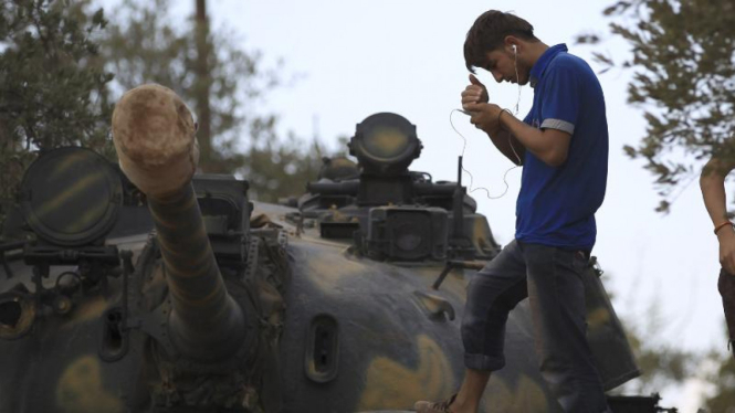 Pejuang FSA sedang melihat ponselnya di atas tank di Hama, Suriah.