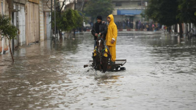 Warga Palestina mengendari kuda untuk melalui jalan yang terendam banjir.
