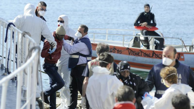 Penjaga pantai membantu imigran turun dari kapal di pelabuhan Sisilia.