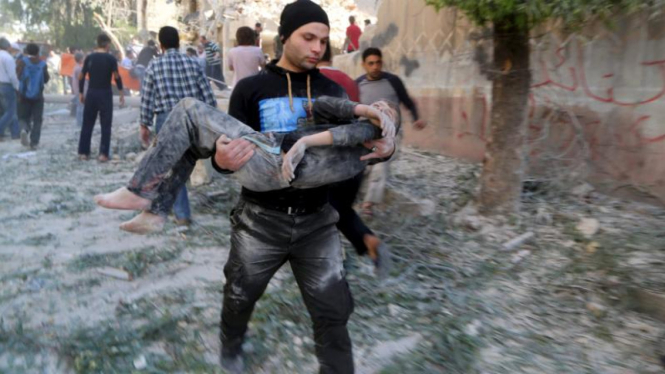 Seorang pria memanggul remaja yang terluka di Aleppo.
