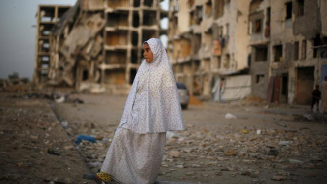 Gadis Palestina berdiri dengan bangunan yang hancur akibat serangan Israel.