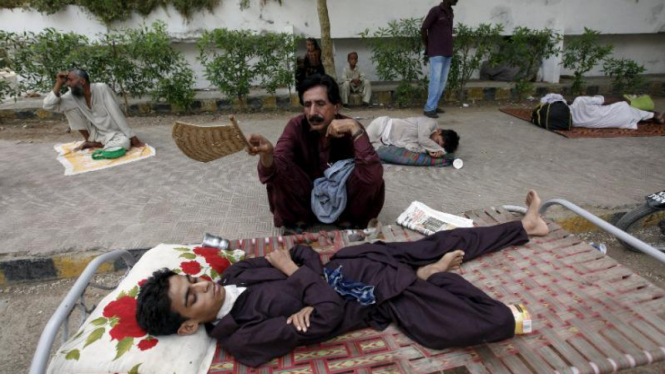 Ayah mengipasi putranya, menunggu pemeriksaan dokter di Pakistan.
