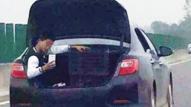 Seorang pria berfoto selfie di bagasi mobil
