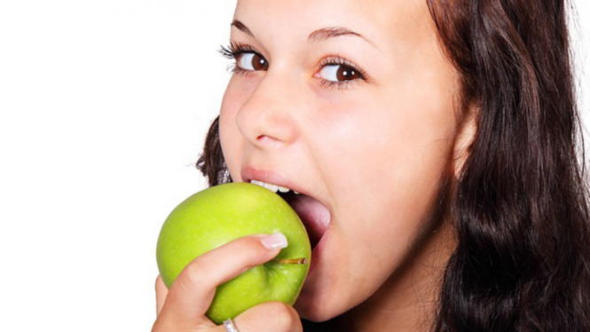 Wanita makan buah apel.
