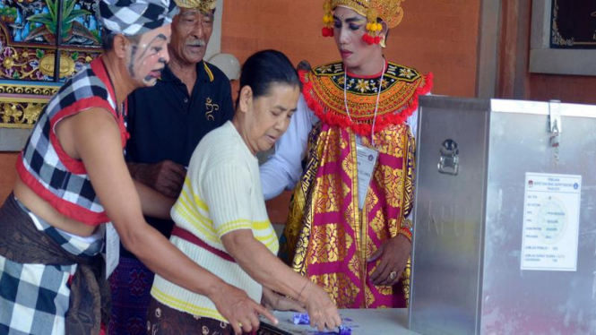 Anggota Kelompok Penyelenggara Pemungutan Suara (KPPS) mengenakan busana penari dan pelawak Bali membantu pemilih saat pemungutan suara di Desa Penarungan, Badung, Bali