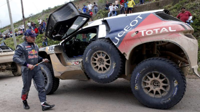 Pengendara Peugeot Carlos Sainz berjalan dekat mobilnya di Reli Dakar 2016.