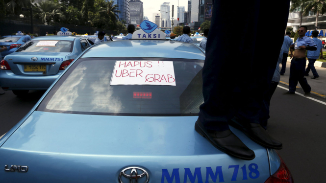 Pengendara taksi ini berdiri di atas mobilnya sendiri saat melakukan unjuk rasa menentang transportasi online di jalan utama ibukota Jakarta, Selasa (22/03/2016).