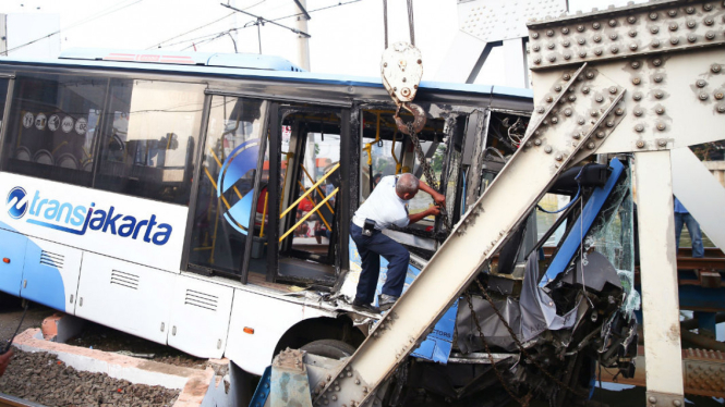 Petugas evakuasi Bus TransJakarta yang ditabrak kereta Senja Utama di perlintasan Gunung Sahari, Kamis kemarin.