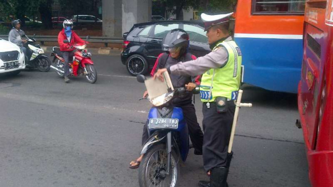 Petugas memberi sanksi tilang ke pengendara motor yang masuk jalur TransJakarta.