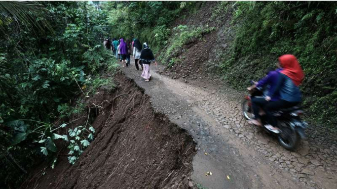 Warga melintasi jalan yang sebagian runtuh menuju lokasi longsor di Desa Gumelem Kulon, Susukan, Banjarnegara, Jawa Tengah, Minggu (19/6/2016).