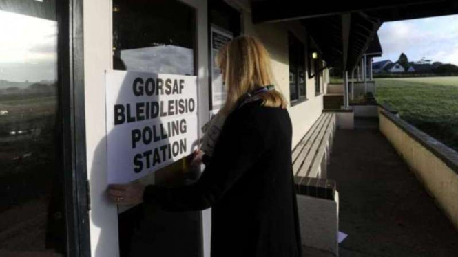 Seorang wanita menempel papan informasi bilik suara di Desa St. Florence, Wales.
