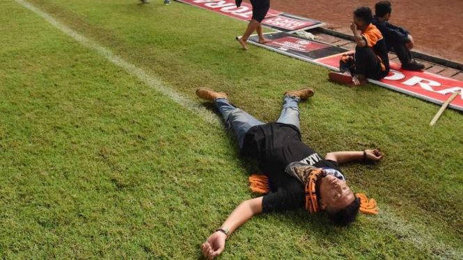 Suporter Persija Jakarta tergeletak akibat asap tembakan gas air mata ketika terlibat kericuhan dengan petugas kepolisian pada laga Torabika Soccer Championship di Stadion Utama Gelora Bung Karno, Jakarta, Jumat (24/6). 