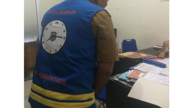 Seorang PNS di Kabupaten Gorontalo yang dikenakan sanksi atas keterlambatannya dengan mengenakan jaket anti terlambat bergambar jam dinding besar, Kamis (4/8/2016)