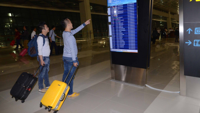 Para penumpang memperhatikan jadwal keberangkatan pesawat mereka di bandara.