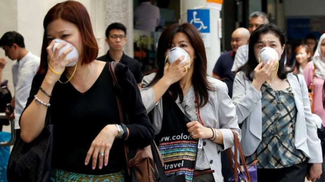 Warga Singapura menutupi hidung dengan masker saat menghadapi polusi kabut asap pada 2016. 