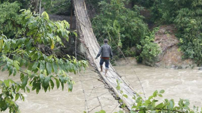 Seorang warga Dusun Cadas Bodas Garut nekat menyeberangi jembatan gantung yang nyaris ambruk akibat diterjang arus sungai, Senin (19/9/2016)