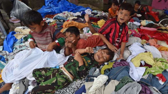 Bocah korban banjir bandang sungai Cimanuk bermain di atas baju sumbangan.