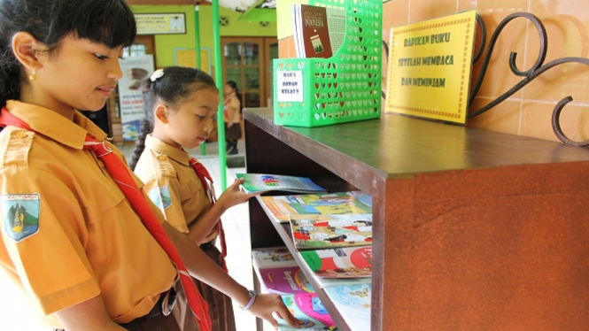 Dua sahabat perpustakaan sedang menyusun buku di rak sekolah.