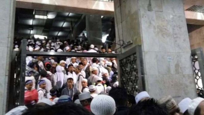 Massa yang belum bisa masuk masjid Istiqlal berjejalan di tangga pintu masuk.