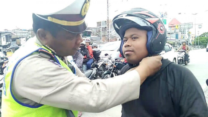 Petugas polisi ajarkan penggunaan helm yang tepat ke pengendara motor.