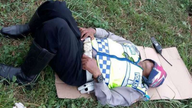 Petugas polisi memanfaatkan waktu istirahat dengan tidur di atas rumput.