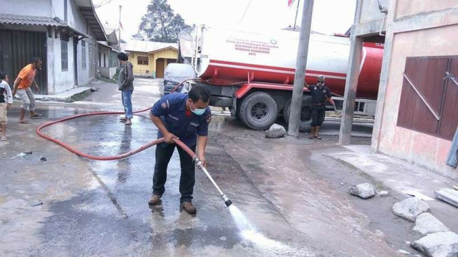 Petugas pemadam bahaya kebakaran Kabupaten Karo membersihkan sisa abu vulkanik Gunung Sinabung yang menutupi permukiman warga, Senin (7/8/2017)