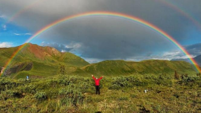 Pria berpose di dekat pelangi.