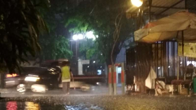 Seorang juru parkir mengatur kendaraan parkir saat hujan lebat guyur Surabaya.