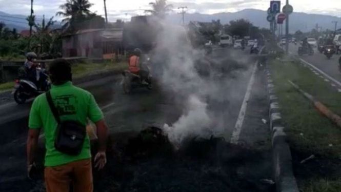 Petugas membersihkan material ban sehabis dibakar dalam aksi blokade jalan By Pass di Padang, Sumatera Barat, pada Kamis pagi, 14 Desember 2017.
