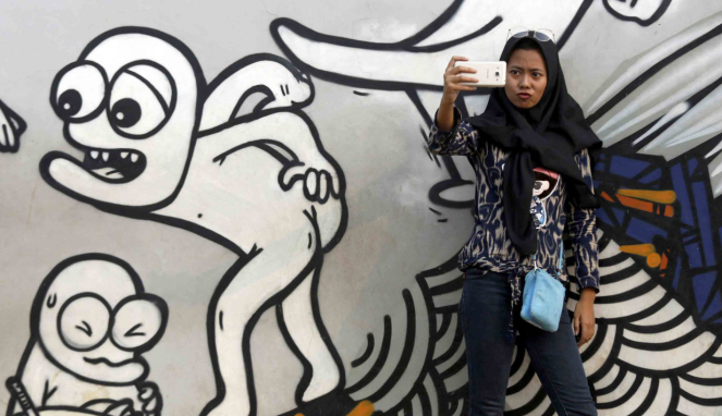 Seorang gadis sedang selfie dengan latar lukisan mural di Jakarta