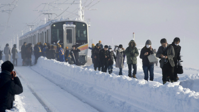 Para penumpang turun dari kereta setelah menginap semalaman di dalam kereta karena terjebak salju.
