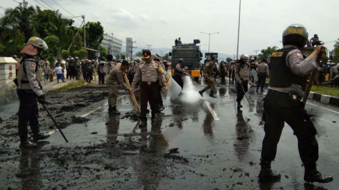 Polisi membersihkan material ban-ban bekas yang dibakar massa dalam aksi unjuk rasa di jalan by pas Kota Padang, Sumatra Barat, pada Jumat, 26 Januari 2018.