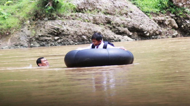 Kastopo membantu anaknya menyeberangi sungai untuk sekolah
