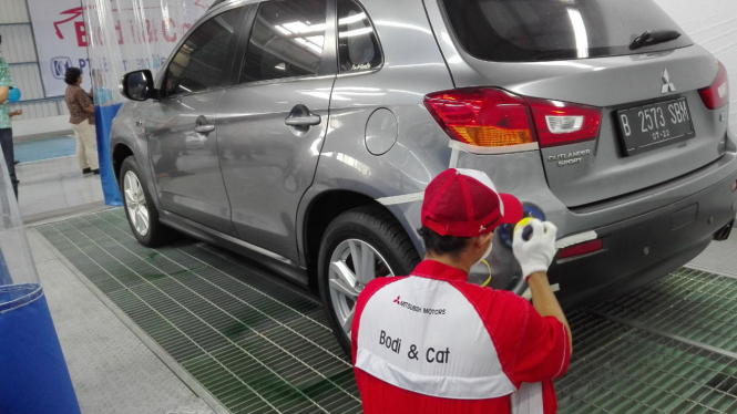 Pekerja sedang memerbaiki bodi mobil Mitsubishi.