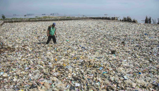 Petugas kebersihan berjalan di antara tumpukan sampah di kawasan teluk Jakarta