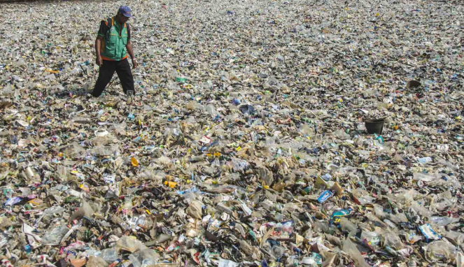 Petugas kebersihan berjalan di antara tumpukan sampah di kawasan teluk Jakarta