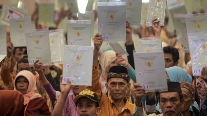 Sejumlah warga mengangkat sertifikat tanah mereka usai diserahkan oleh Menteri Agraria dan Tata Ruang Sofyan Djalil pada 2018