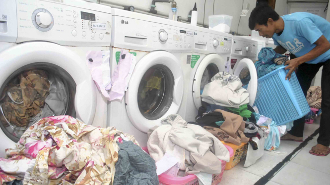 Pekerja memasukkan pakaian ke dalam mesin cuci di Bogor Laundry, Kota Bogor
