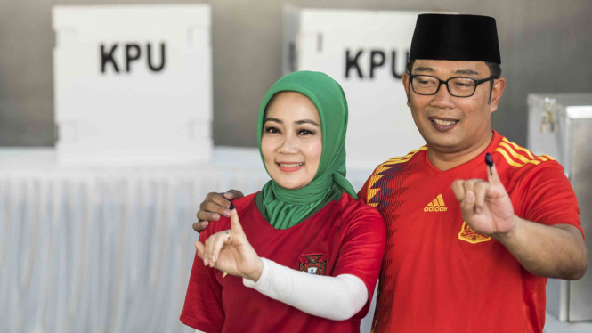 Calon Gubernur Jawa Barat nomor urut satu Ridwan Kamil (kanan) bersama istri Atalia Praratya (kiri) menunjukkan tinta pada jari seusai menggunakan hak pilih di Pilgub Jabar