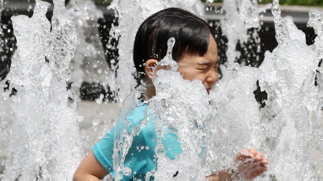 Seorang anak mendinginkan tubuh di pancuran air yang terletak di Plaza Gwanghwamun Seoul. - YONHAP/EPA