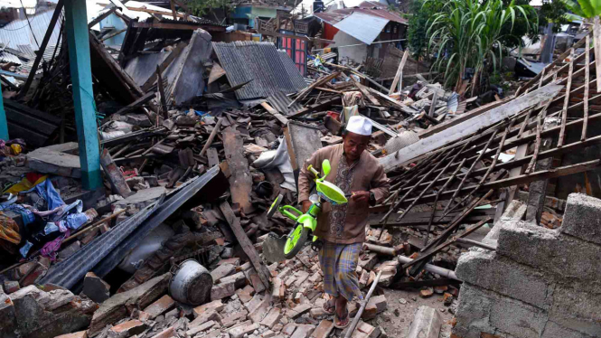 Warga mengangkat sepeda dari reruntuhan rumah yang rusak akibat gempa bumi di Lombok Barat, NTB