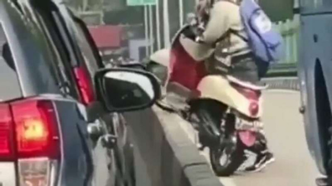 Pengendara mengangkat motor melewati beton pembatas.