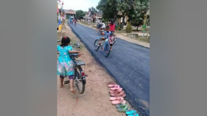 Anak-anak melepas sandal saat bermain di jalan yang baru diaspal.