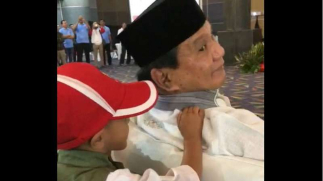 Seorang bocah bertopi merah memijat pundak Prabowo Subianto saat sang calon presiden berpidato di hadapan para petinggi partai koalisi Indonesia Adil Makmur di Jakarta, pada Minggu, 23 September 2018.