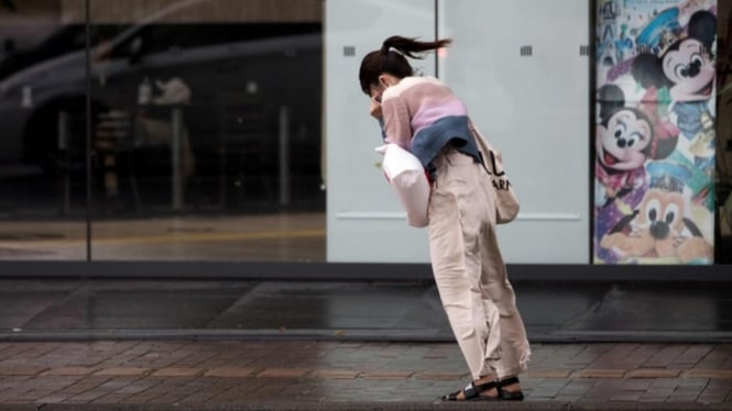 Seorang perempuan berjalan melawan arah angin di Kota Kagoshima, Jepang, selagi Topan Trami melanda pada Minggu (30/9). - AFP/Getty Images